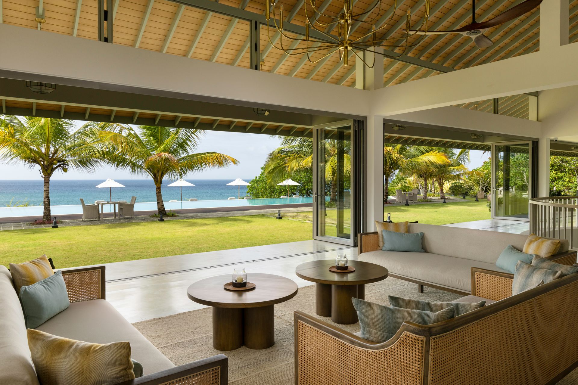 The lounge, with rattan sofas and round wooden tables, opening onto a lawn, palms, the pool and the sea